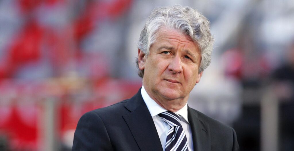 Moderator Marcel Reif im schwarzen Jacket mit weißem Hemd und Krawatte im Fußballstadion.