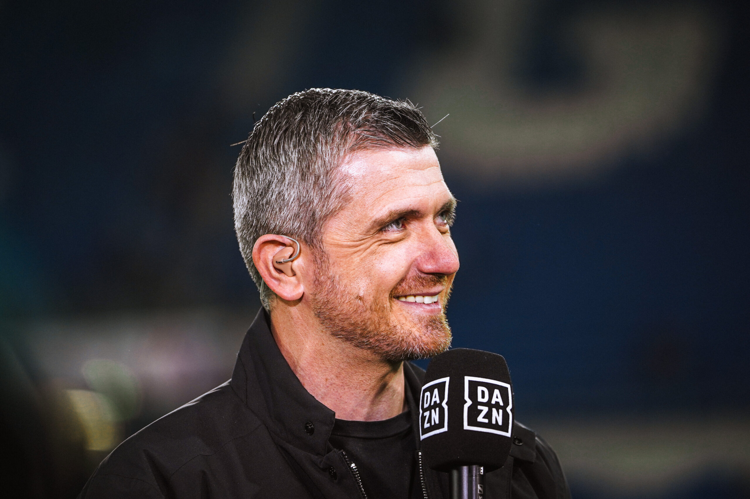 Moderator Sebastian Kneissl in schwarzer Jacke mit DAZN Mikrofon.